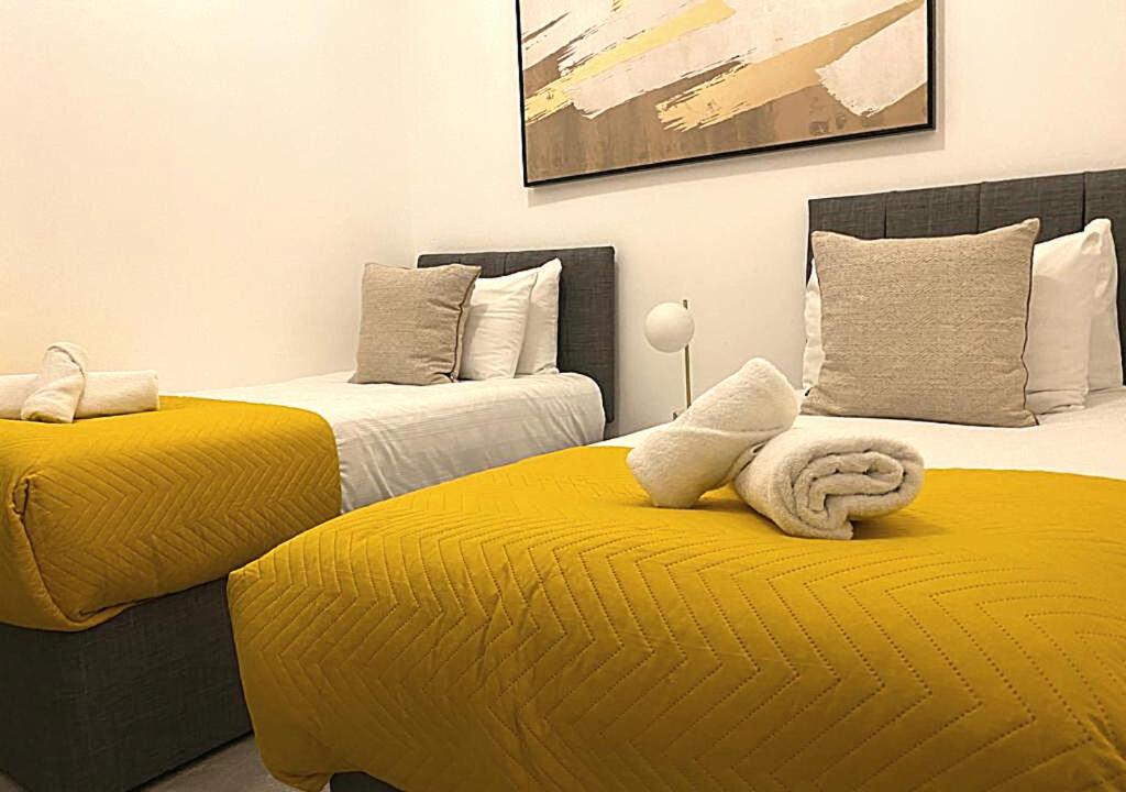 two beds with yellow sheets in a room at Samdel Camden Charles Suite in London