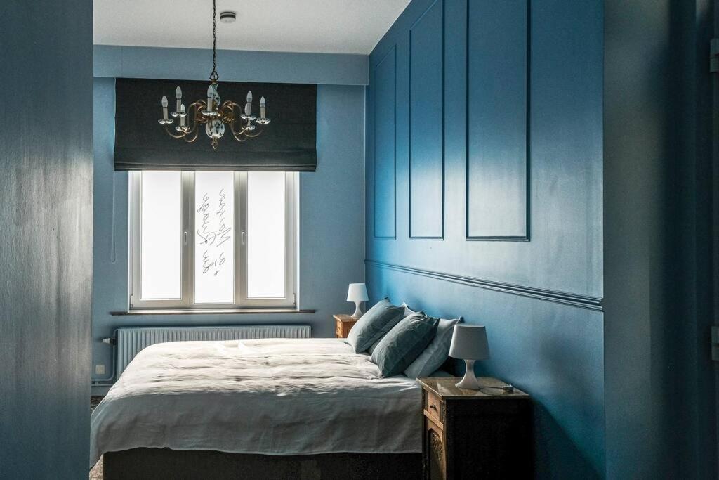 een slaapkamer met blauwe muren en een bed met een kroonluchter bij La Maison du Rivage in Dinant
