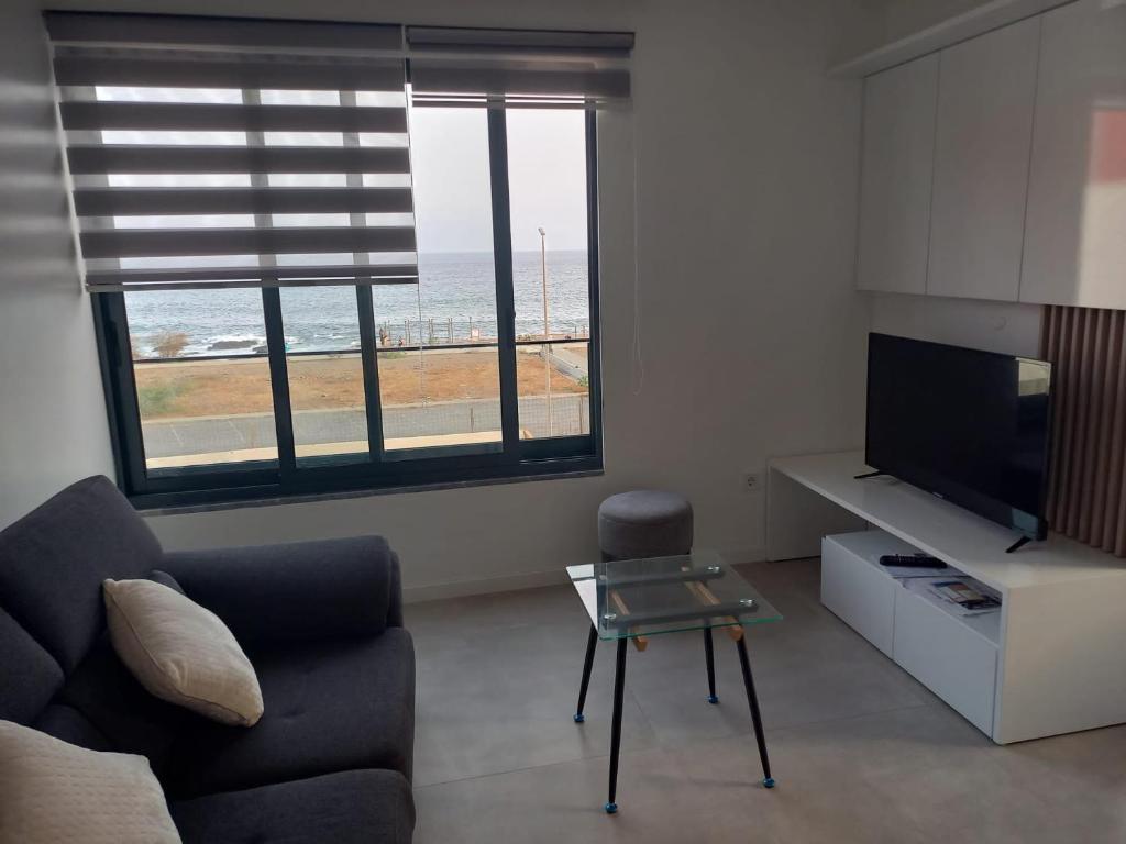 Una sala de estar con un sofá y un televisor y una ventana. en La Calicia - Residência Marina, en Praia