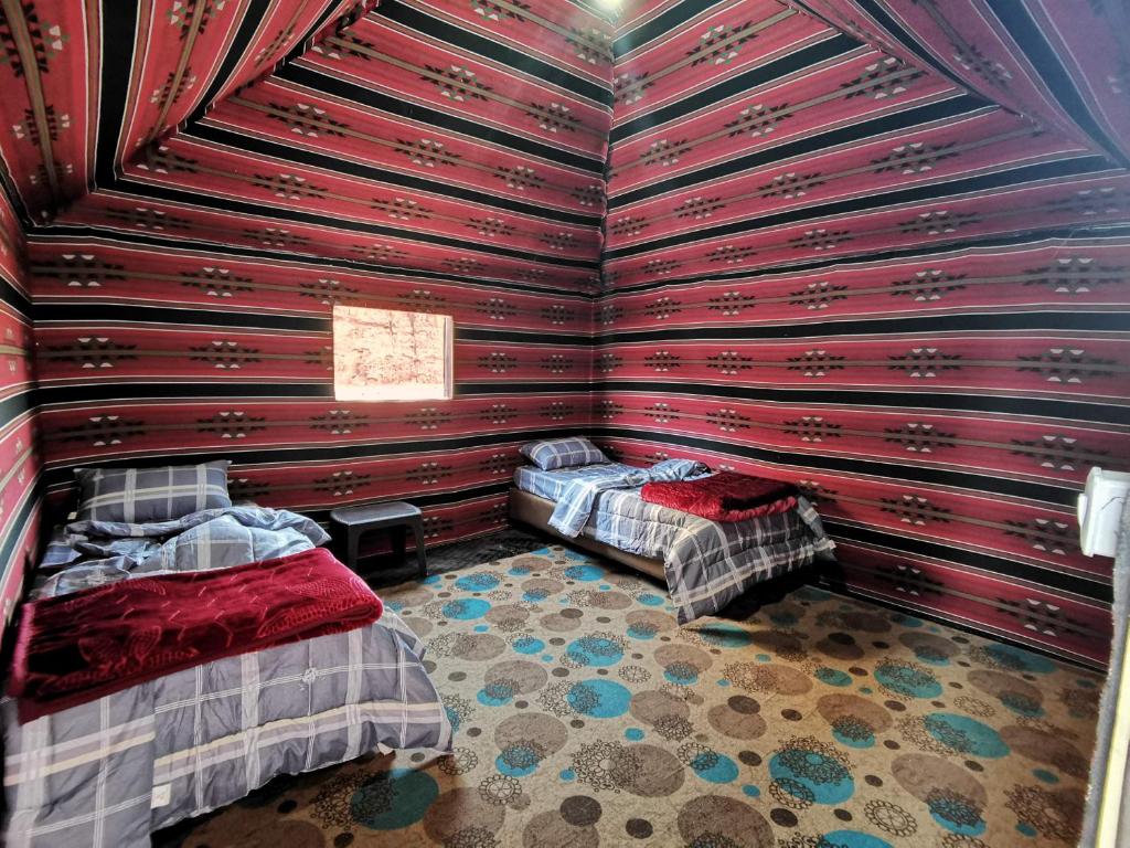 a bedroom with two beds in a room with red walls at Wadi Rum Originality Camp in Wadi Rum