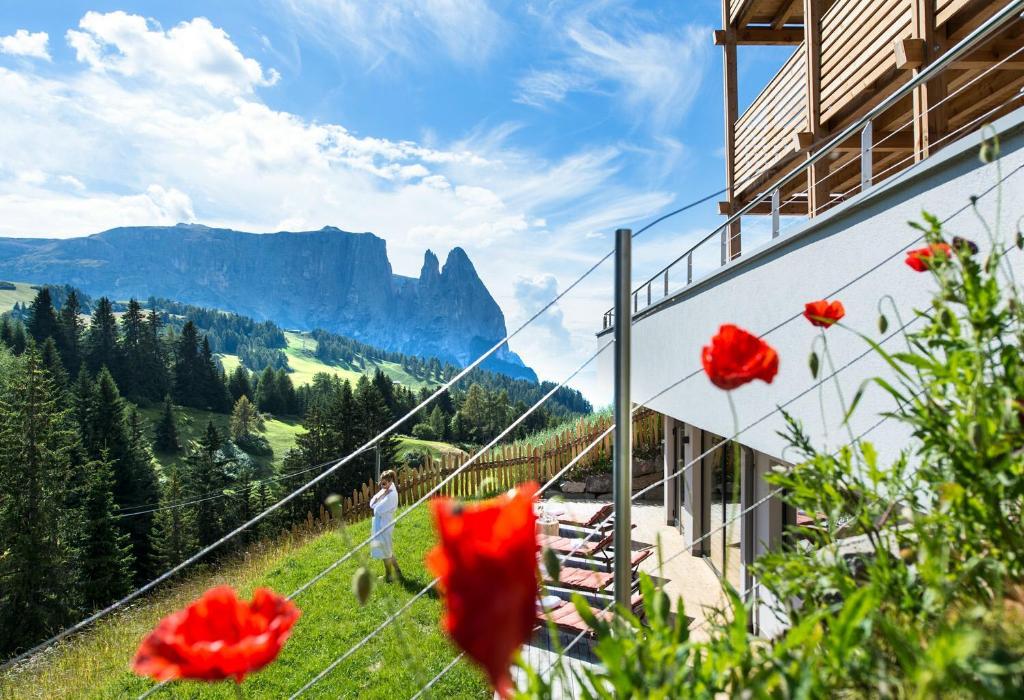 Ein Mann steht auf der Seite eines Berges mit roten Blumen. in der Unterkunft Hotel Chalet Dolomites in Alpe di Siusi