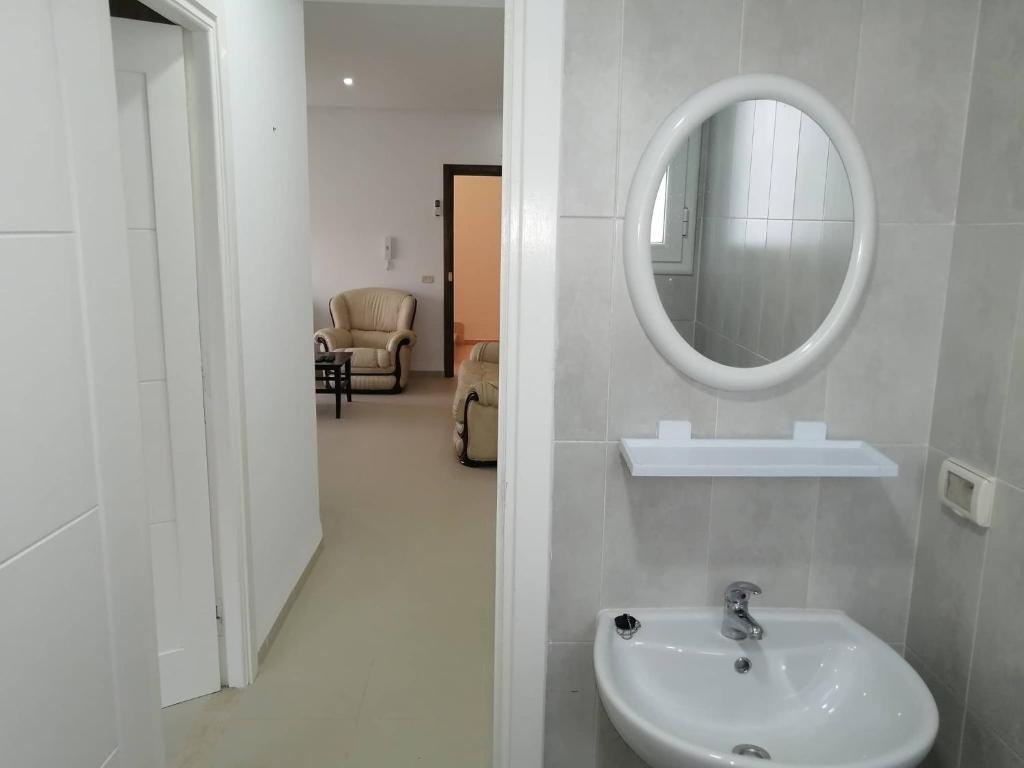 ein Bad mit einem Waschbecken und einem Wandspiegel in der Unterkunft Résidence le corail de chat meriem in Sousse