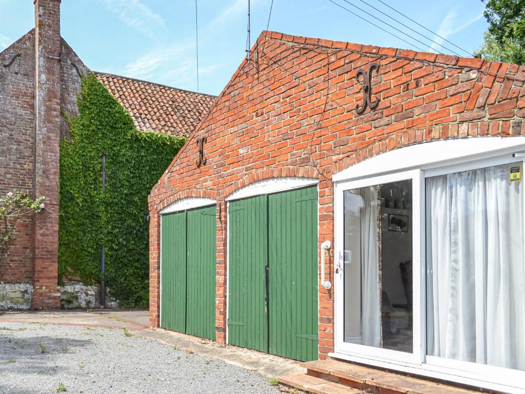 a brick building with green garage doors and ivy at The Old Farm Cottage in Louth