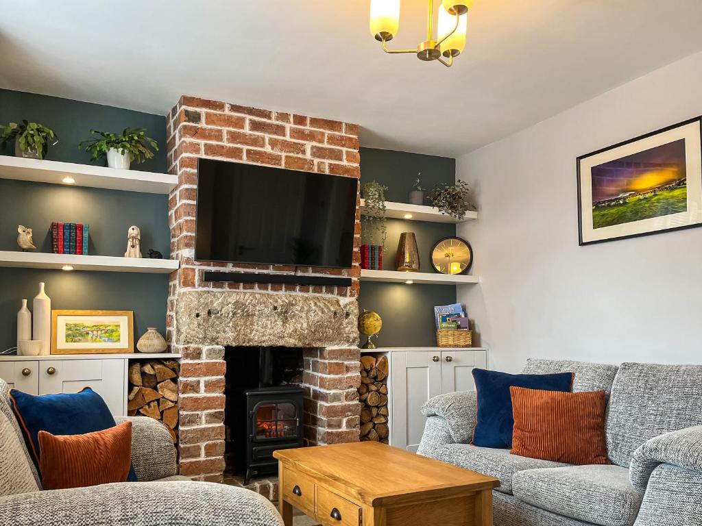 a living room with a brick fireplace with a flat screen tv at Red Robin Cottage in Wingerworth