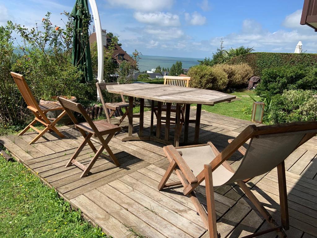 een houten tafel en stoelen op een terras met een parasol bij Grand rez de jardin-terrasse avec vue sur la mer - 2 chambres in Blonville-sur-Mer
