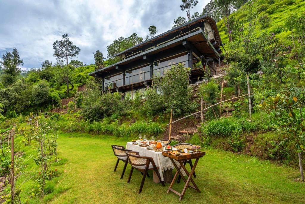 a table with chairs and a house on a hill at StayVista at Leopard's Creek with Pool in Solan