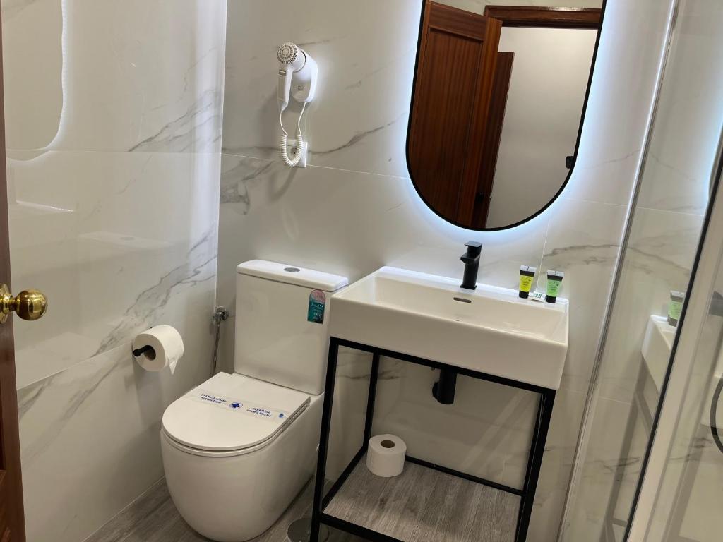 a bathroom with a toilet and a sink and a mirror at H Pelayo Auto Check-In Rooms in Noja