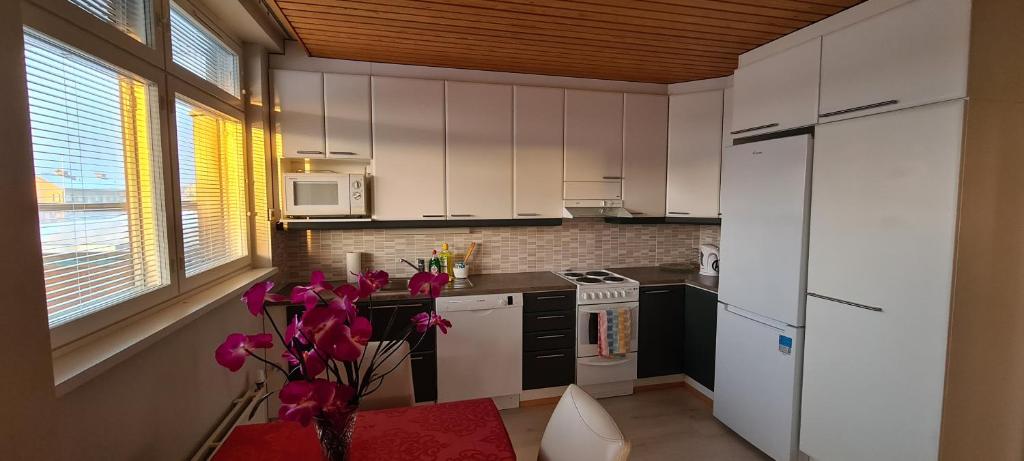 a kitchen with white cabinets and pink flowers in a vase at Kattohuoneisto keskustassa in Lieksa