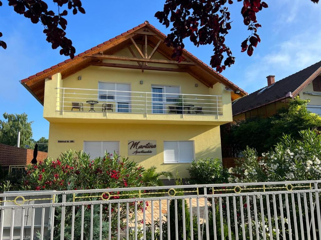 żółty dom z białym płotem przed nim w obiekcie Martina Apartmanház w mieście Balatonlelle