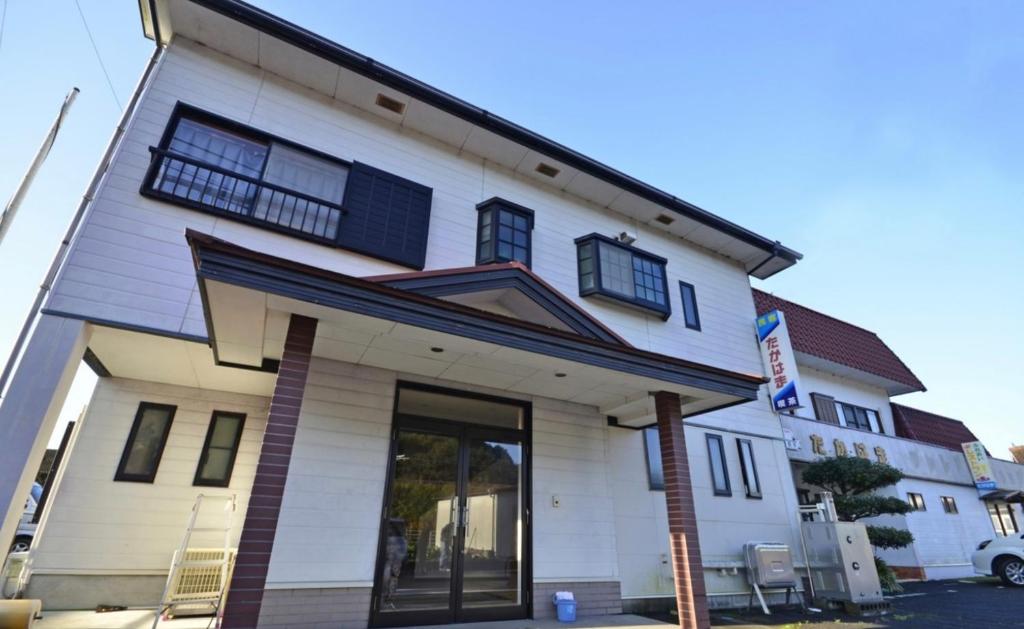 ein weißes Haus mit schwarzen Fenstern auf einer Straße in der Unterkunft 民宿たかはま Takahama Guest house 