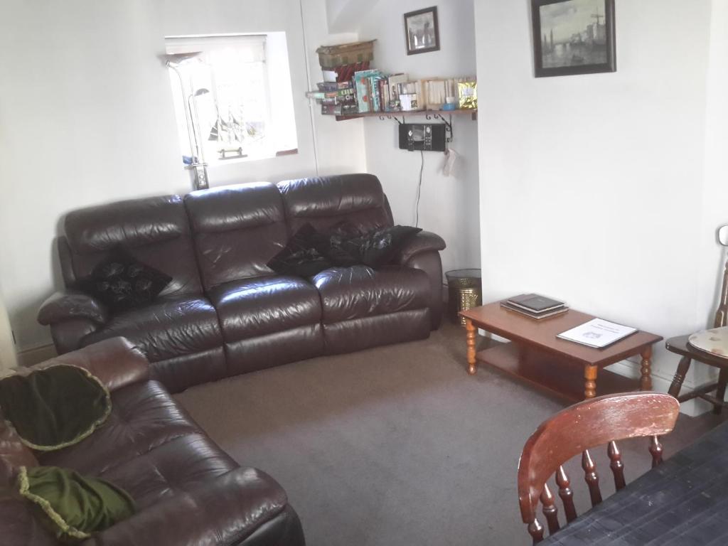 ein Wohnzimmer mit einem Ledersofa und einem Tisch in der Unterkunft Lupine Cottage in Whitby