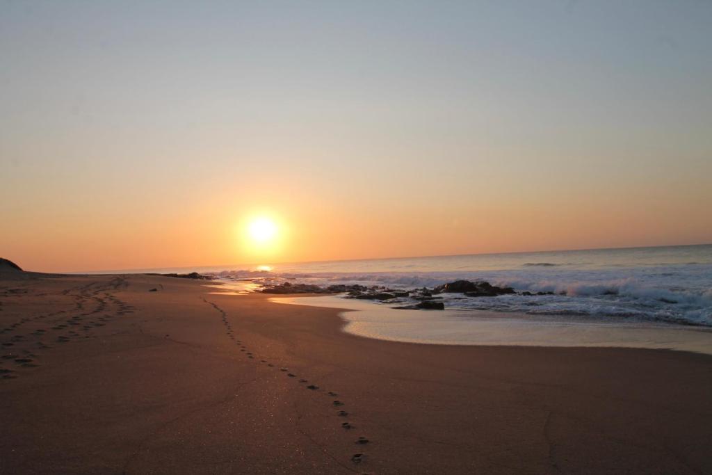 a sunset on the beach with footprints in the sand at Villa Plaza in Shelly Beach