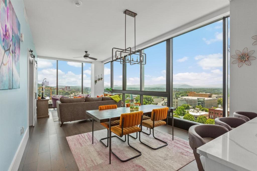 a living room with a table and chairs and large windows at 'Endless Sunset Retreat' A Luxury Downtown Condo with Panoramic Mountain Views at Arras Vacation Rentals in Asheville