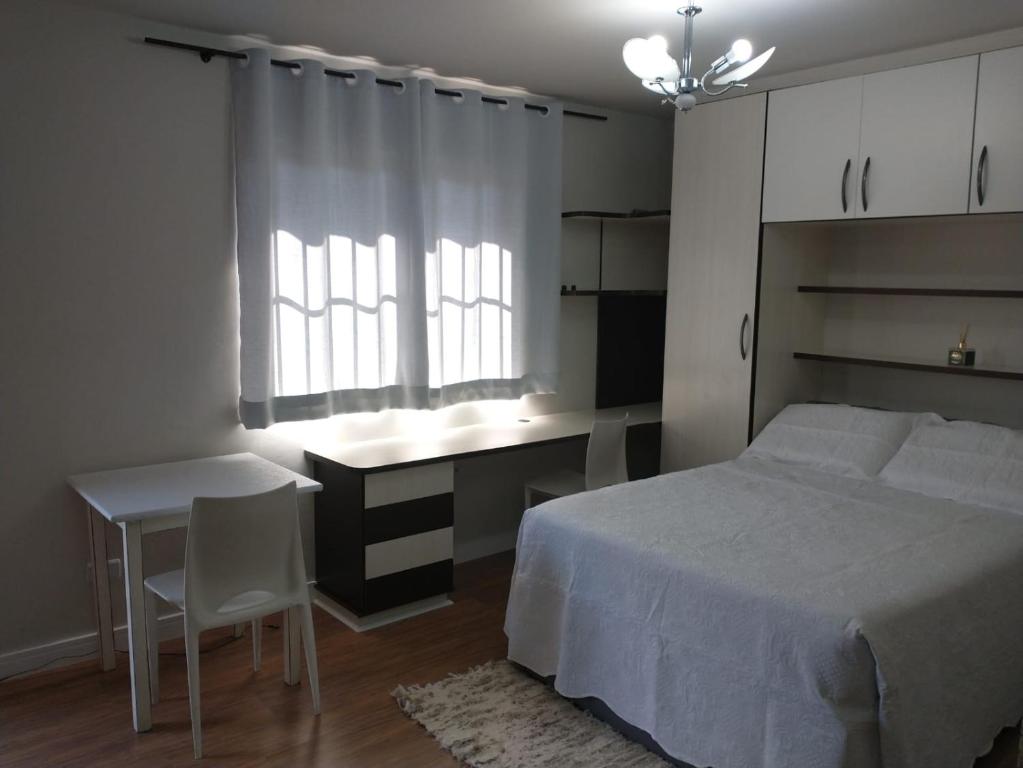 um quarto com uma cama, uma secretária e uma janela em Residencial Vitor Studio 5 em São José dos Pinhais