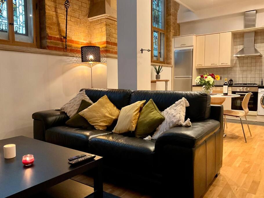 a living room with a black leather couch and a table at Magical Church Conversion in Watford in Watford