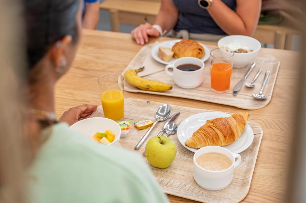 a woman sitting at a table with breakfast foods and drinks at UCPA SPORT STATION HOSTEL PARIS in Paris