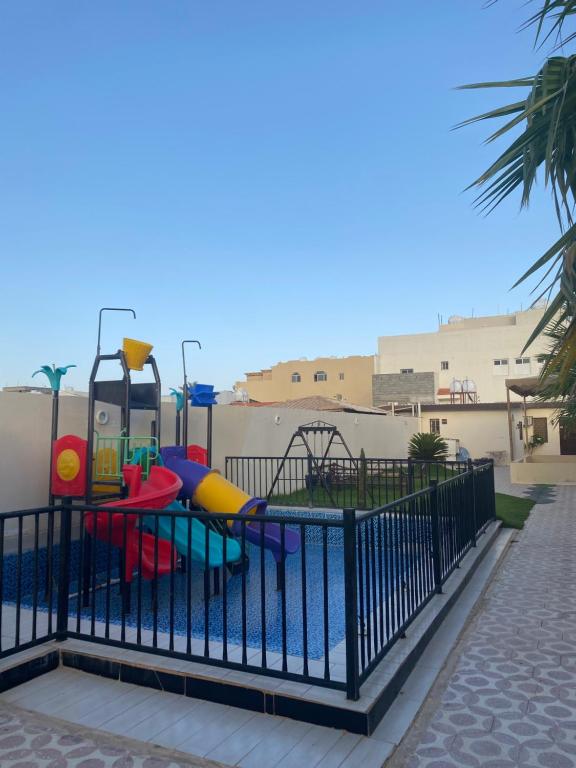 einen Spielplatz hinter einem Zaun neben einem Pool in der Unterkunft ليلتنا in Ha'il