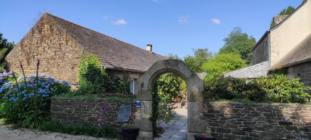 ein altes Steingebäude mit einem Bogen und Blumen in der Unterkunft Gîte - Les Pivoines Les Jardins de Kerellec 20min de la mer 4 à 6 personnes terrasse in Plouvorn