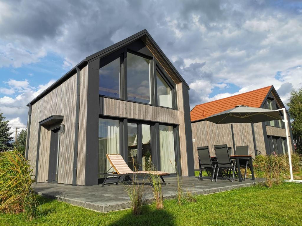 a small house with a deck with chairs and an umbrella at Binibona Barn Haven Rydzewo in Rydzewo