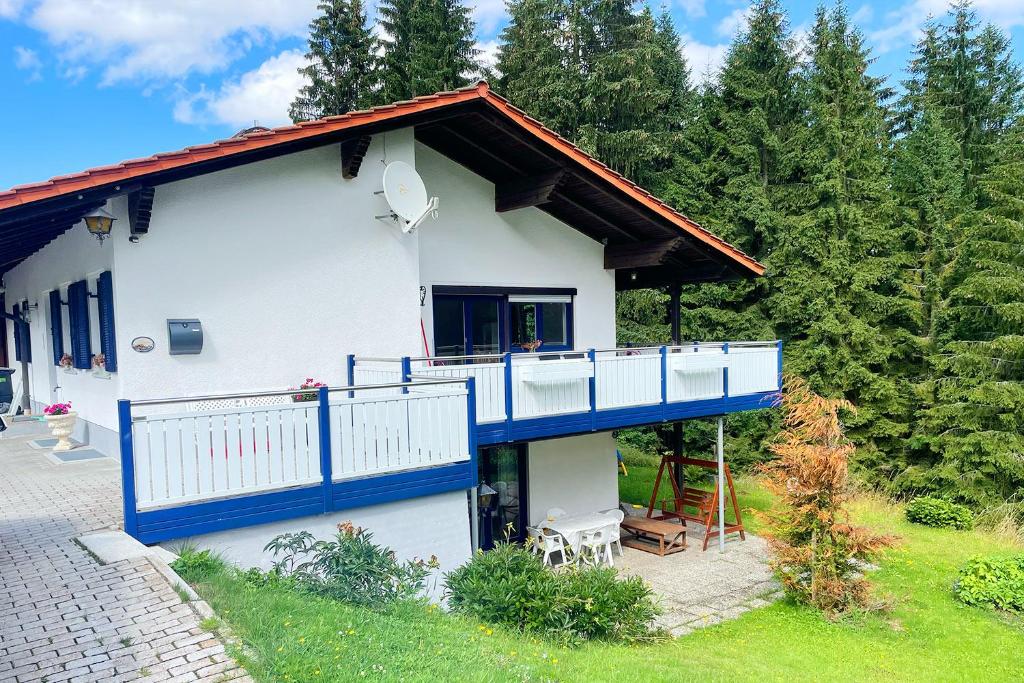 uma casa branca com uma varanda azul e árvores em Haus Waldblick em Philippsreut