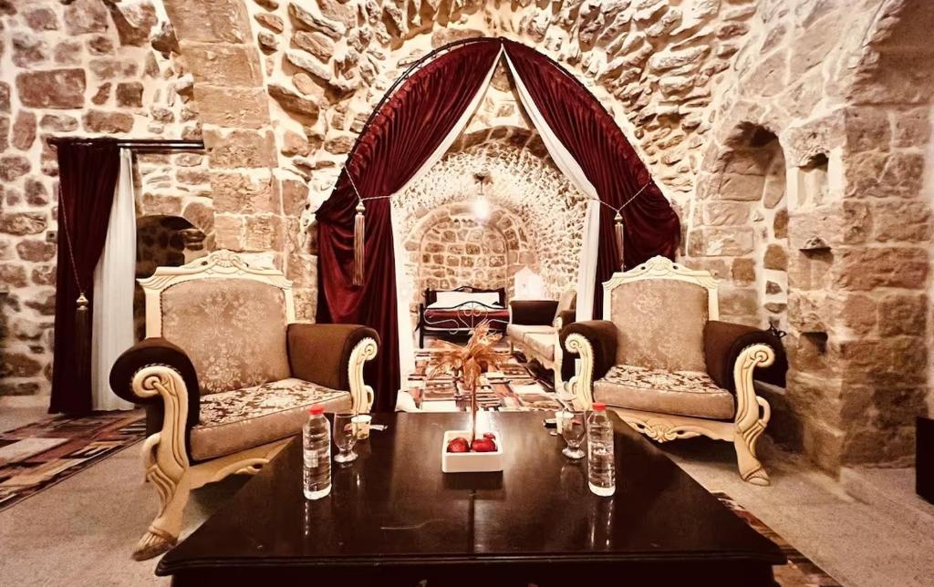 ein Wohnzimmer mit einem Tisch, 2 Stühlen und einer Steinmauer in der Unterkunft Acabey Konuk Evleri in Mardin
