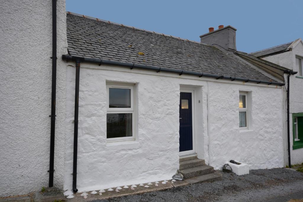 a white house with a black door and stairs at Seal Cottage in Portnahaven