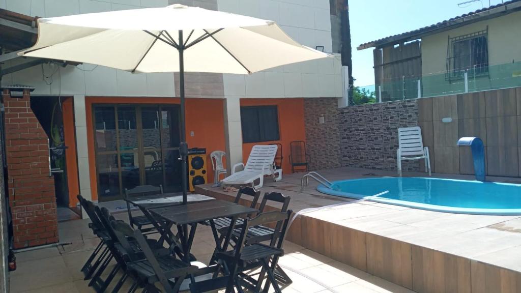 uma mesa e cadeiras com um guarda-sol ao lado de uma piscina em Linda Casa Itamaracá em Jaguaribe