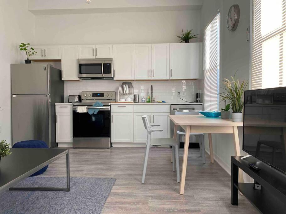 a kitchen with white cabinets and a table and a refrigerator at Chic Bungalow Apartment steps from Armature Works & Downtown Riverwalk in Tampa