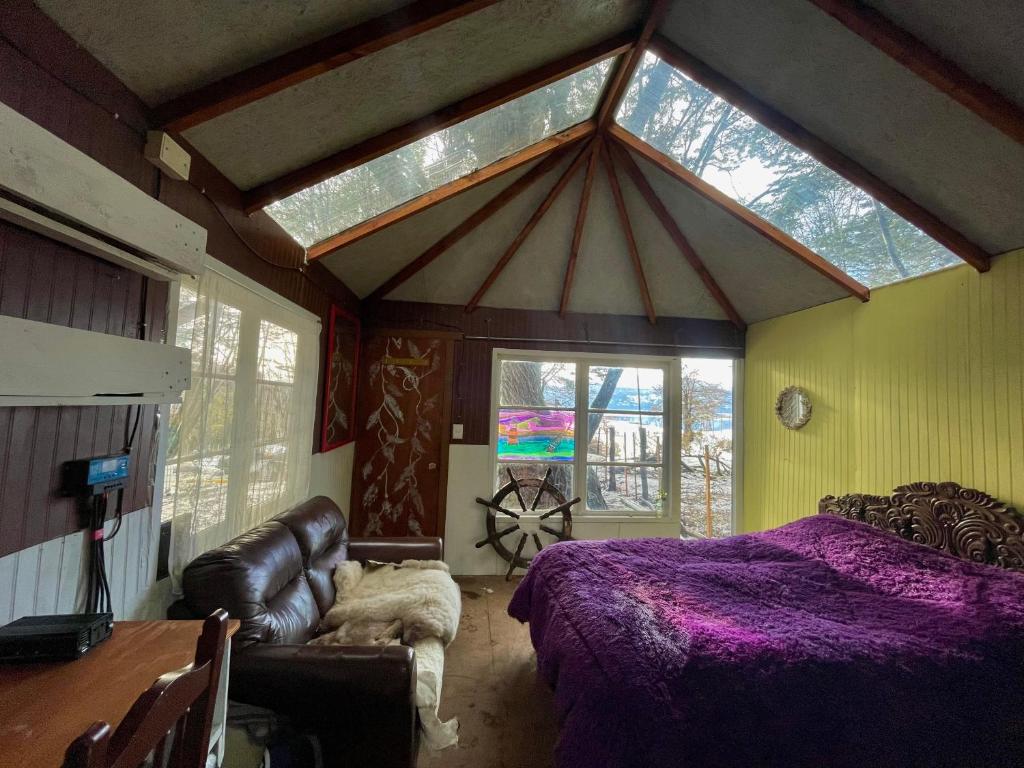 a bedroom with a purple bed and a couch and windows at Refugio El Cauque in Puerto Williams