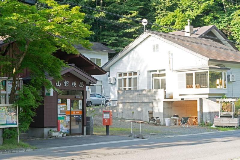 una pequeña casa blanca con un edificio al lado de una calle en 一棟貸宿　奥入瀬屋 en Yakeyama