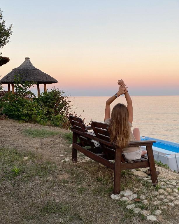 a woman sitting on a bench looking at the ocean at Отдых у моря in Nova Dofinivka
