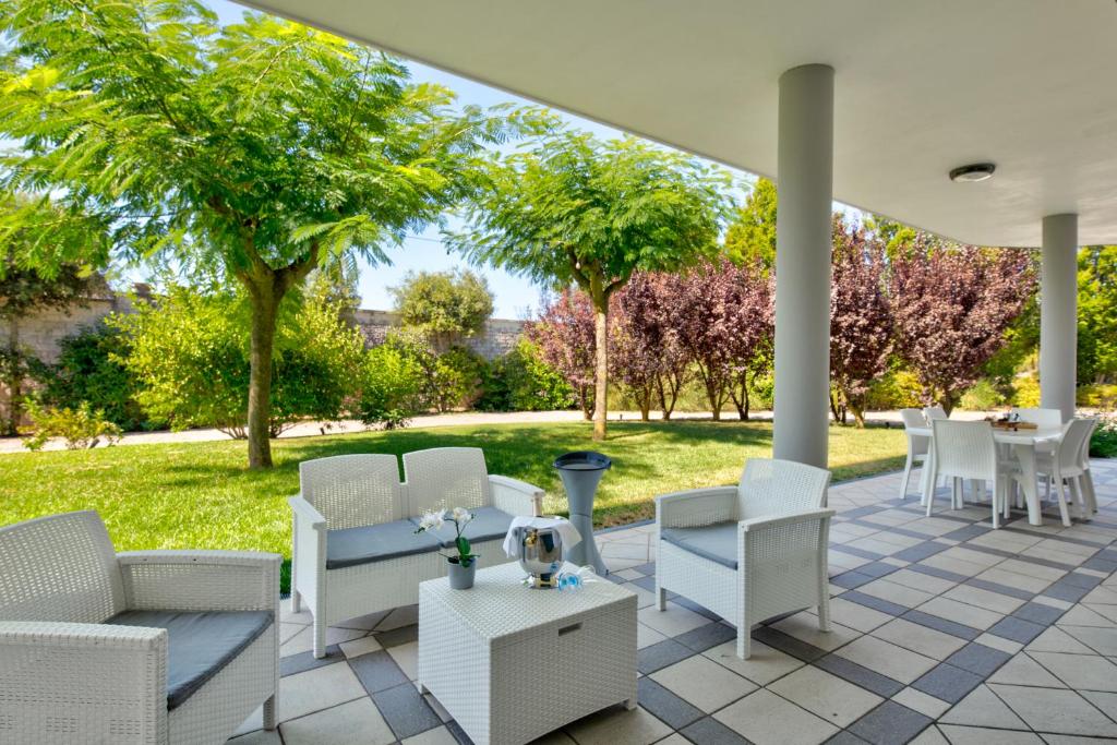 Un patio con sillas y mesas blancas y árboles en Villa Estia - nel cuore della Valle D'Itria, en Cisternino