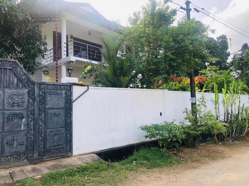 a white fence with a black gate in front of a house at Calm Palace in Weligama