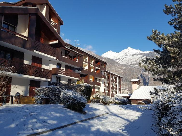un grand bâtiment dans la neige avec des montagnes en arrière-plan dans l'établissement Agréable appartement proche Funiculaire, à Bourg-Saint-Maurice