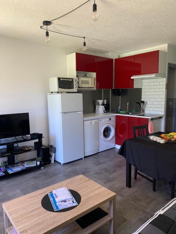 a kitchen with red cabinets and a white refrigerator at Appartement Cosy Tout Confort PARKING AC WIFI LINEN INCLUDED pool access extra in Canet-en-Roussillon