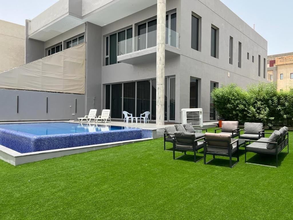 a house with a yard with a swimming pool and green grass at Sama Chalet kuwait in Al Khīrān