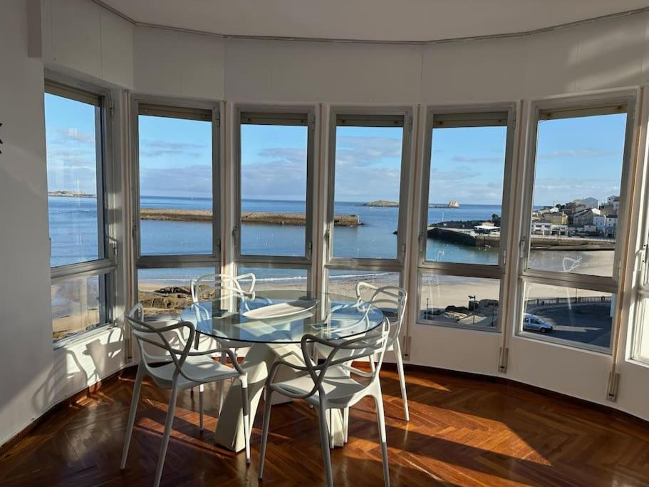 een eetkamer met een tafel, stoelen en ramen bij Piso con vistas al mar. Apartamento Miramar in San Cibrao