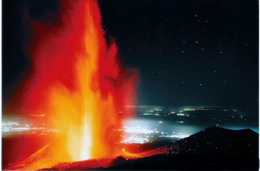 un gran cráter de fuego por la noche con una ciudad en Casa Etna-Mare, en Santa Venerina