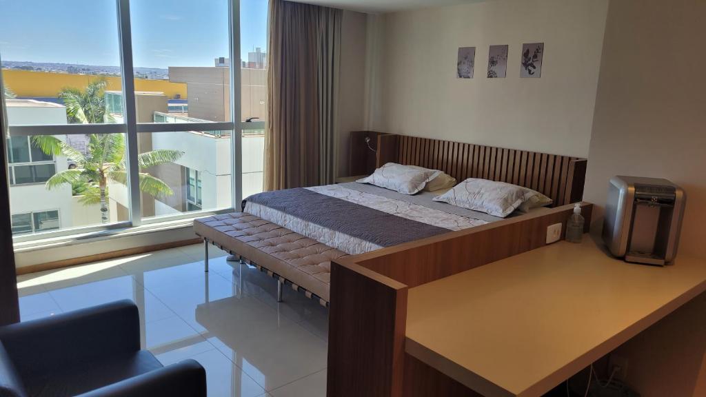 a bedroom with a bed and a desk and a window at Flat no Jade Blue Tree in Brasilia