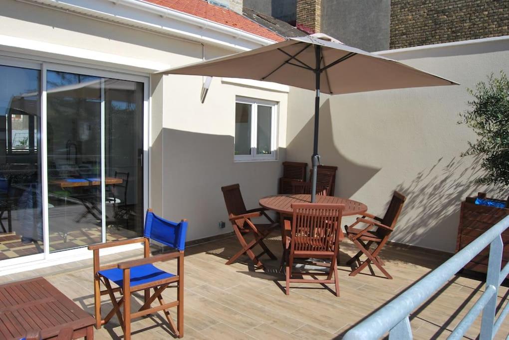 un patio avec une table, des chaises et un parasol dans l'établissement A deux pas de la Mer. Maison avec jardin sud. Les Moussaillons, à Dunkerque