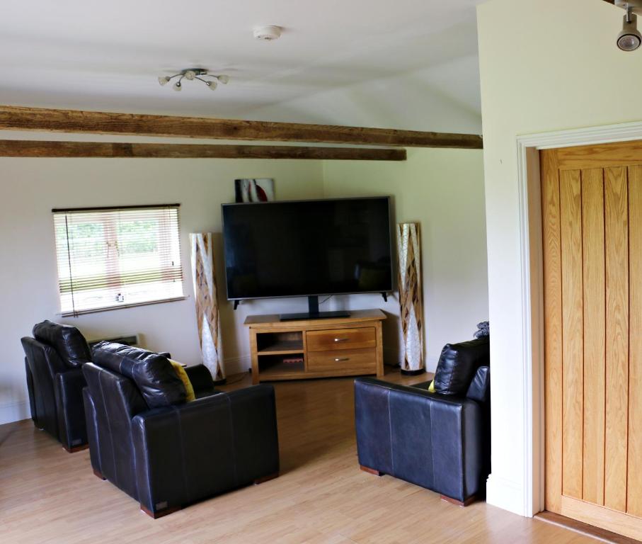 a living room with three leather chairs and a flat screen tv at The Lodge - 2 acres of garden with hot tub and fire pit and BBQ in East Harling