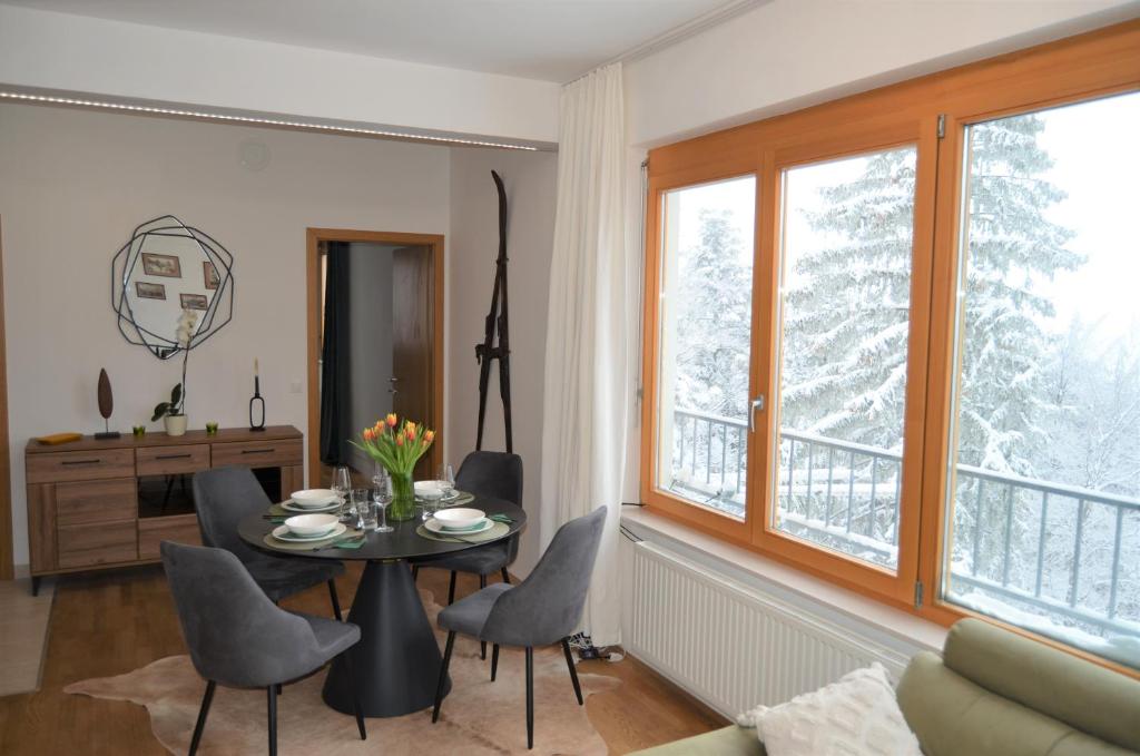 Luxury Wide View Apartment Pohorje Bellevue في هوكو بوهوجري: غرفة معيشة مع طاولة وكراسي ونوافذ
