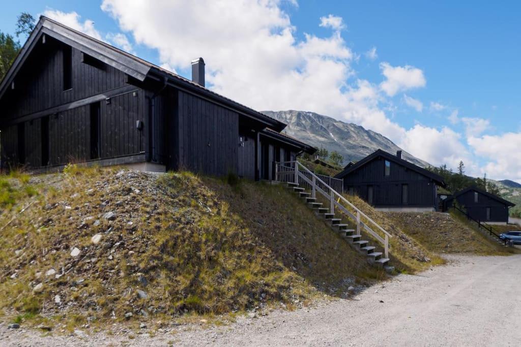 a black building on a hill next to a dirt road at Hovdetunet 77-Gaustablikk in Gaustablikk