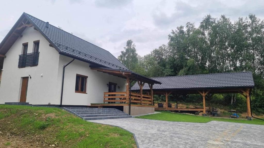 a small white house with a porch and a deck at Domek u Pilota in Ropienka