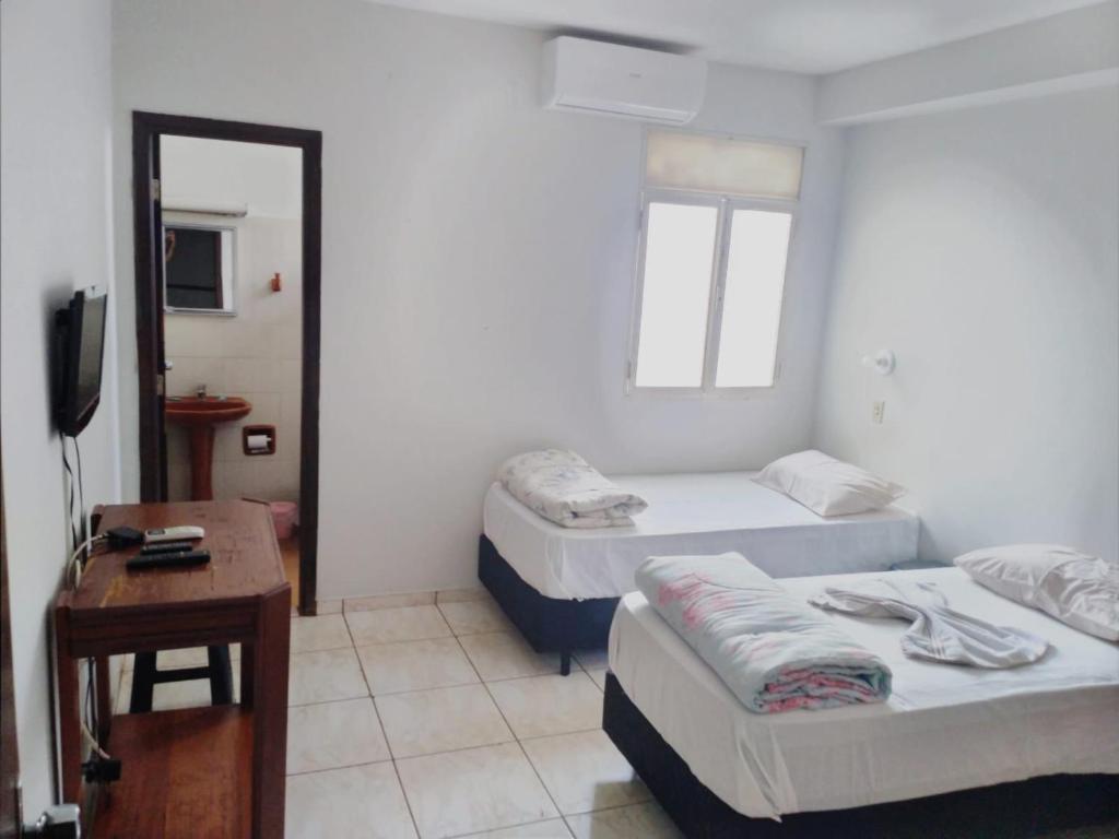 Cette chambre comprend deux lits, une table et une télévision. dans l'établissement ORSI HOTEL, à Araguari
