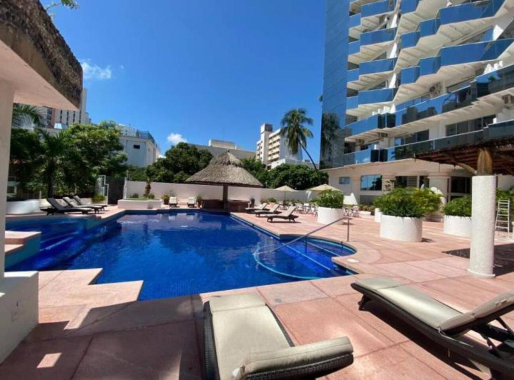 una piscina con tumbonas y un edificio en Fresca estancia en zona Dorada con Alberca/Playa! en Acapulco