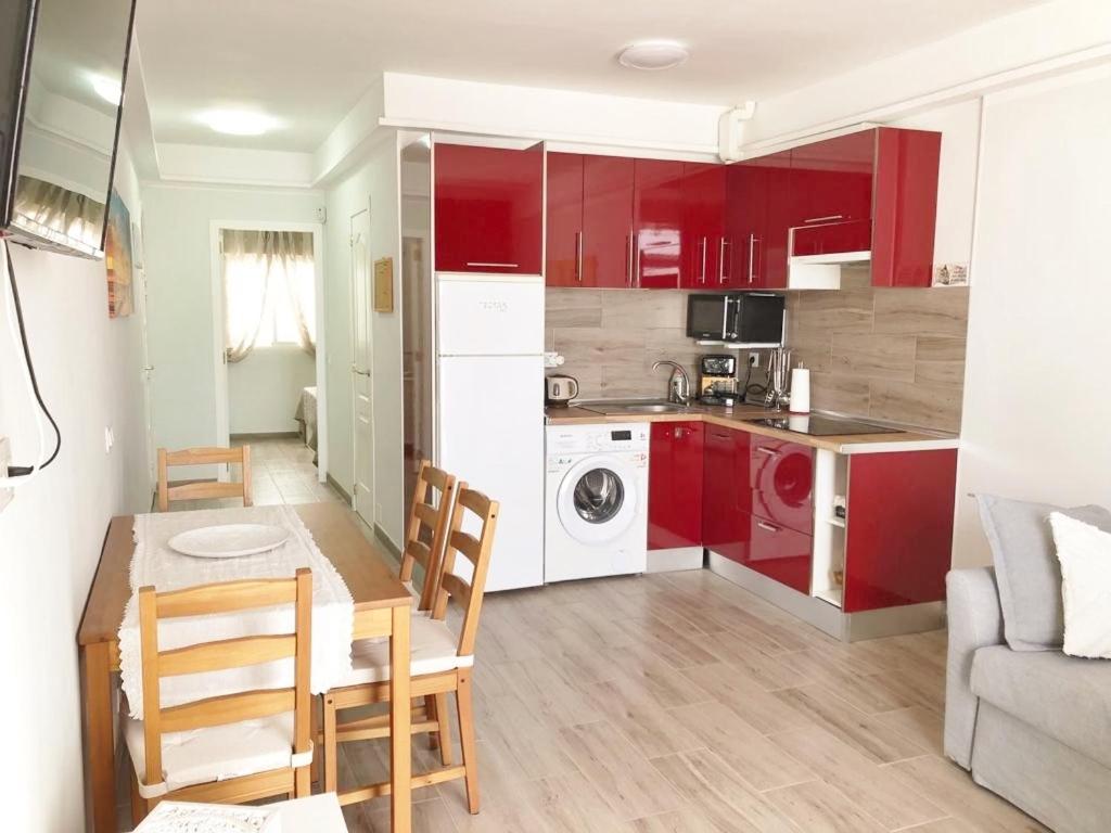 Una cocina y sala de estar con gabinetes rojos y una mesa. en Apartamento Birgitt en Aloha Garden con vista mar y piscina, en Adeje