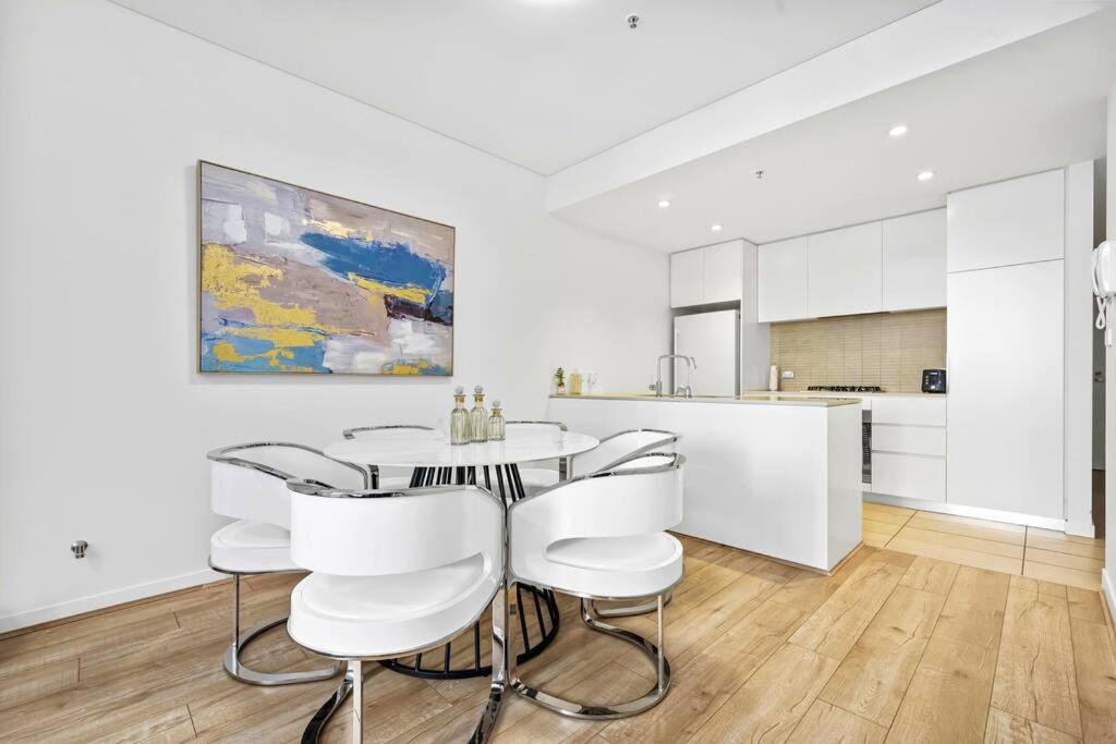 a white kitchen with a table and white chairs at Convenient Modern 2Bed Apt Near Airport in Sydney