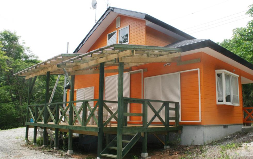 a small orange house with a large deck at コテージ　マリーゴールド in Nasu-yumoto
