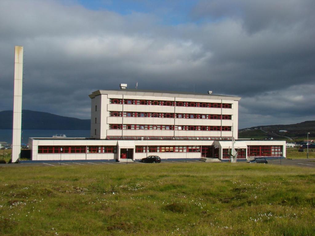 a large white building with a field in front of it at 62N Guesthouse Marknagil in Tórshavn